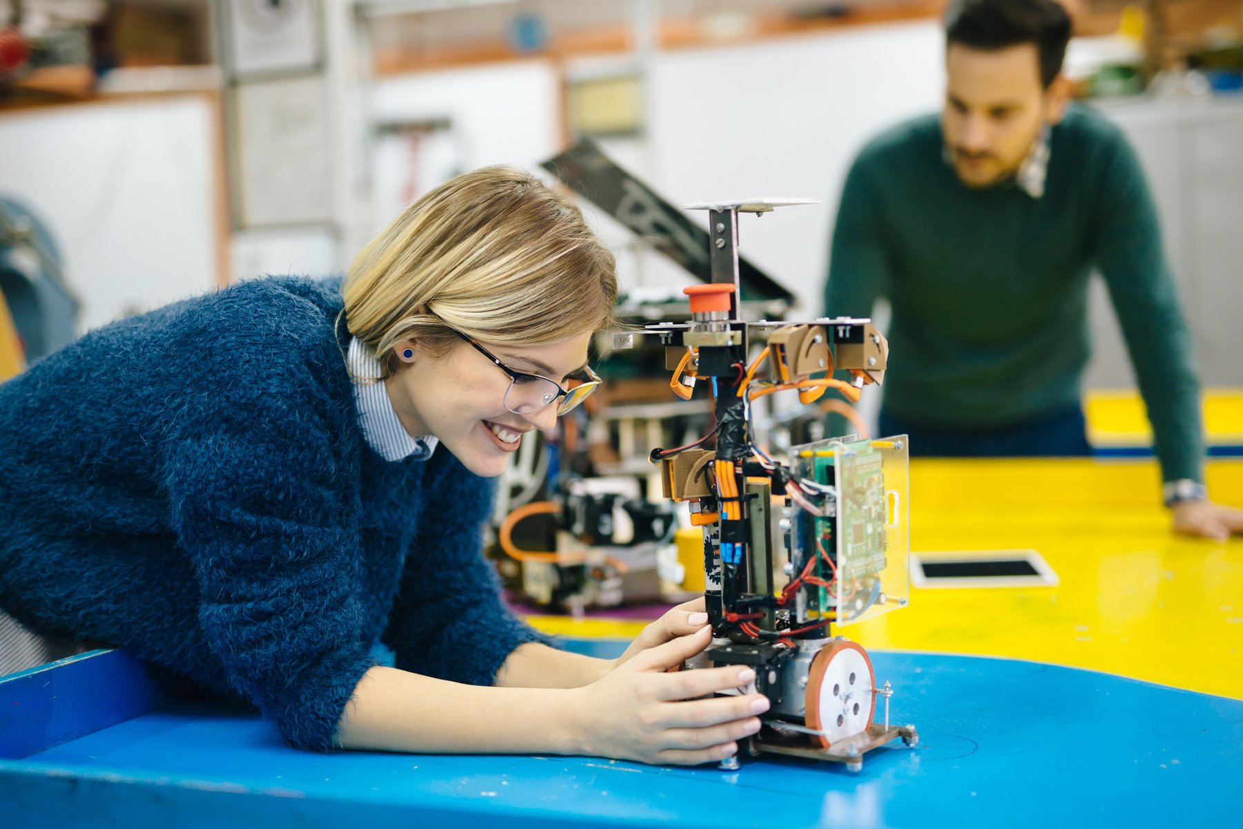 junge Frau beugt sich über selbstgebauten Roboterprototypen mit Kabeln und Drähten