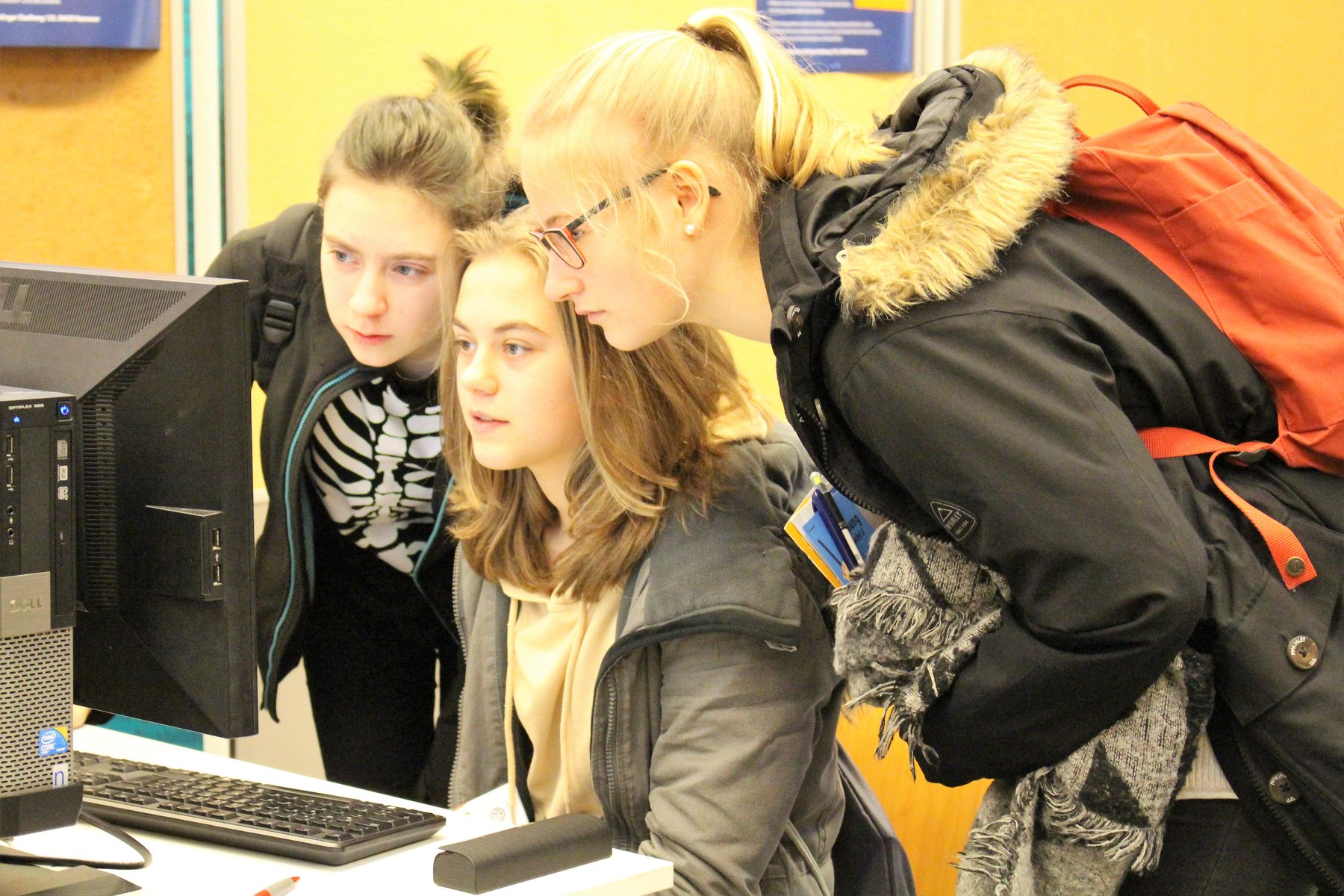 Drei Schülerinnen beugen sich vor einem Computer und suchen erläutern den Inhalt der Bildschirmdarstellung