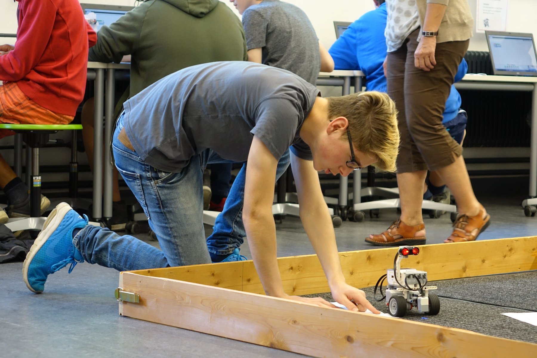 Junger Mann kniet vor Fahrparcours für selbstgebauten Roboter auf Rädern